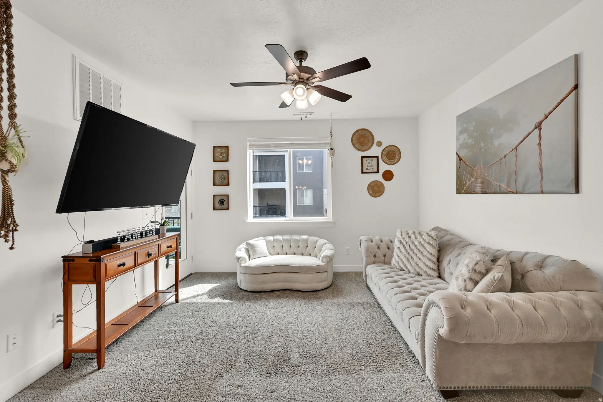 Carpeted living area featuring a ceiling fan with integrated lighting, a wall-mounted television, and a window with natural light