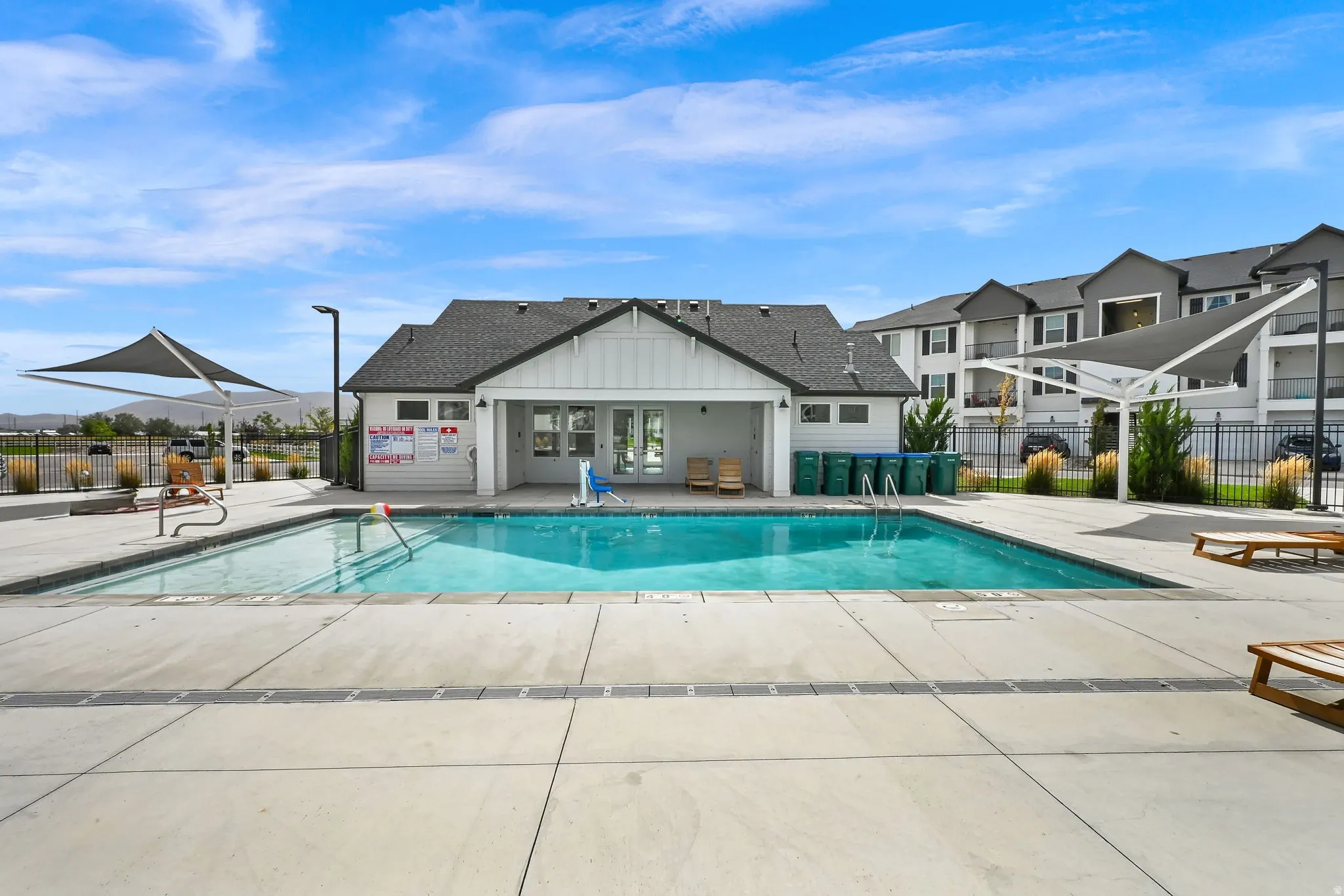 Rectangular swimming pool with surrounding concrete decking, a white-sided pool house, and multiple shade structures