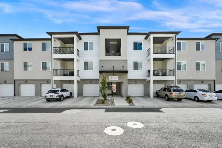 Modern multi-story building featuring individual garage access, private balconies with black railings, and a contemporary facade with varied siding
