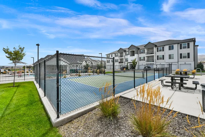 Hard court tennis court with chain-link fencing, adjacent recreational pool, and nearby outdoor dining area