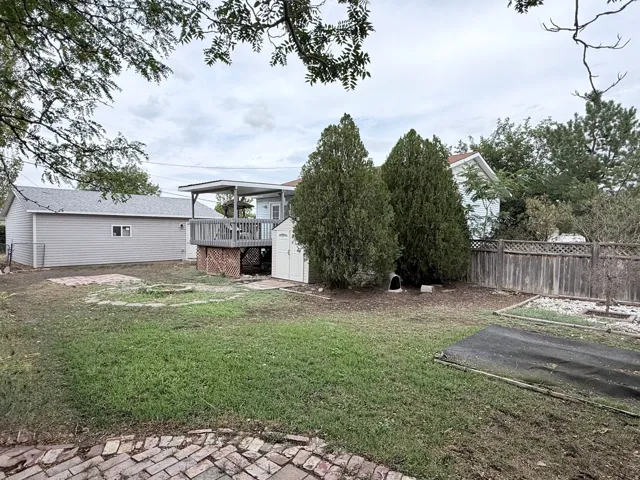 Expansive backyard featuring a covered deck, detached garage with gray siding, and mature perimeter trees