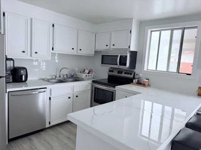 White cabinetry, subway tile backsplash, stainless steel appliances, light-toned wood-finish flooring, and white countertops