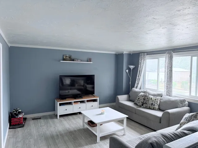 Wood-finish flooring, white trim, multiple windows with white frames, and a floating wall shelf