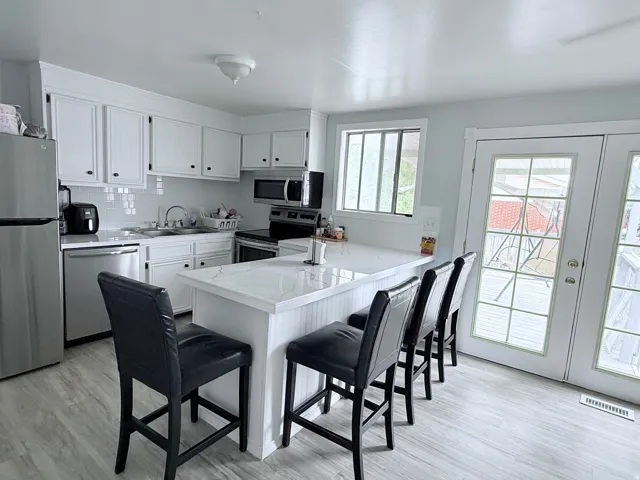 Kitchen featuring white cabinetry with dark hardware, a white tile backsplash, stainless steel appliances, and an island with a white countertop