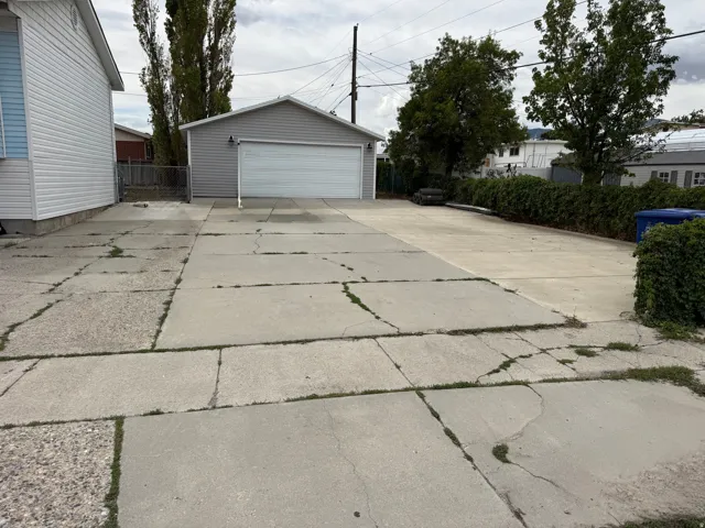 Detached garage with a white overhead door, concrete driveway, and mature landscaping