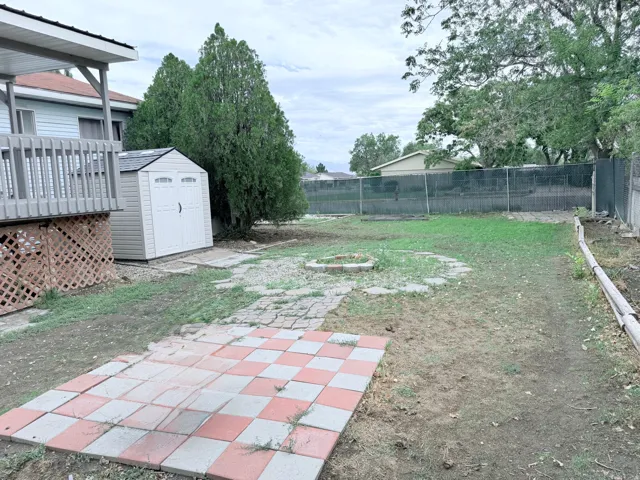 Expansive backyard featuring a checkered patio, a storage shed, a wooden deck, and mature trees