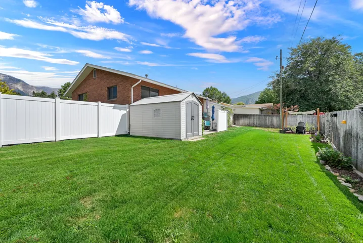 Expansive green lawn with a white privacy fence and a storage shed
