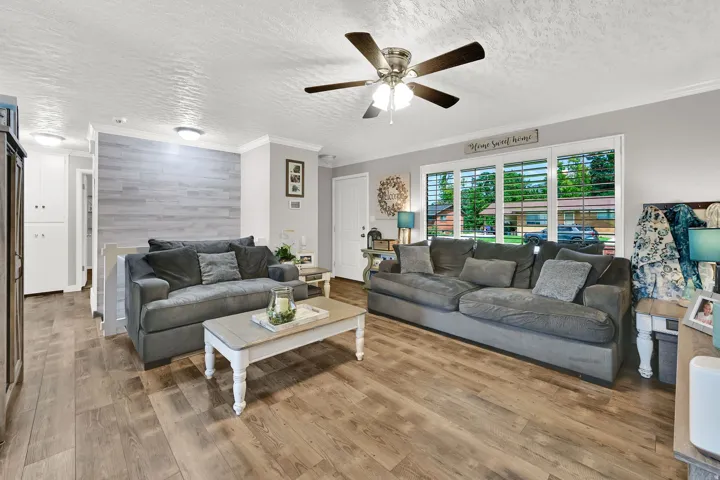 Wood-finish flooring throughout, ceiling fan with integrated lighting, white window blinds, and white trim molding