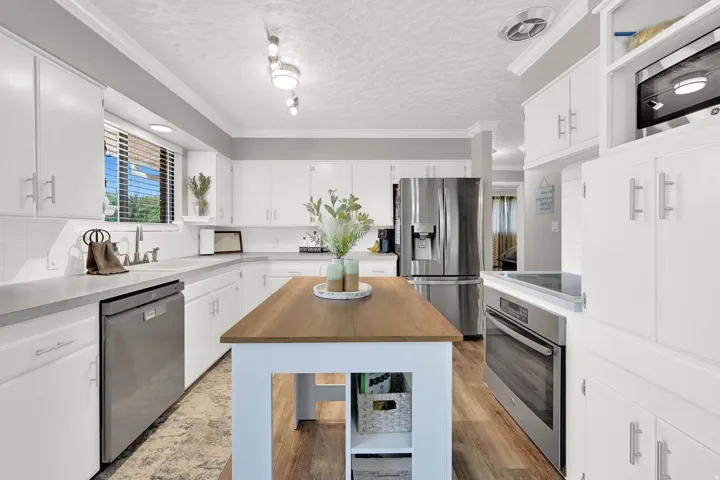 White cabinetry, stainless steel appliances, wood-finish flooring, white subway tile backsplash, and an island with a butcher block countertop
