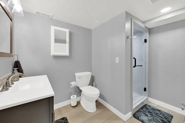 Vanity with integrated sink, glass-enclosed shower with black hardware, white built-in medicine cabinet, and wood-finish flooring