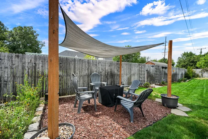 Outdoor seating area with a shade sail, surrounded by a wood privacy fence and a manicured lawn
