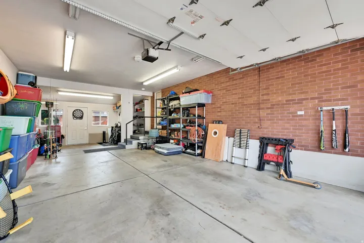 Concrete flooring, brick accent wall, overhead fluorescent lighting, automatic garage door opener, and interior access door