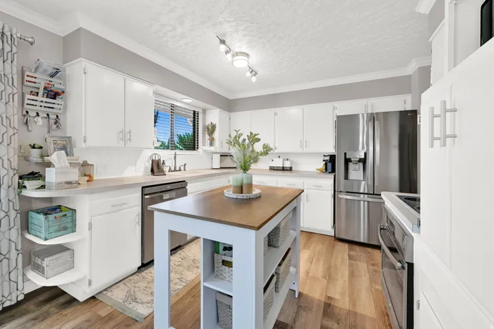 Kitchen featuring wood-finish flooring, white cabinetry, a built-in dishwasher, a stainless steel refrigerator, and a freestanding island with a wood-finish countertop