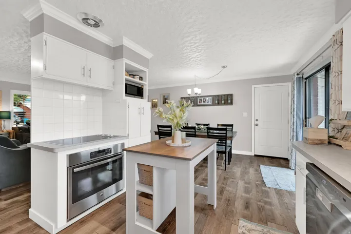 Stainless steel oven and cooktop, white subway tile backsplash, white cabinetry, wood-finish flooring, and a dining area with a chandelier