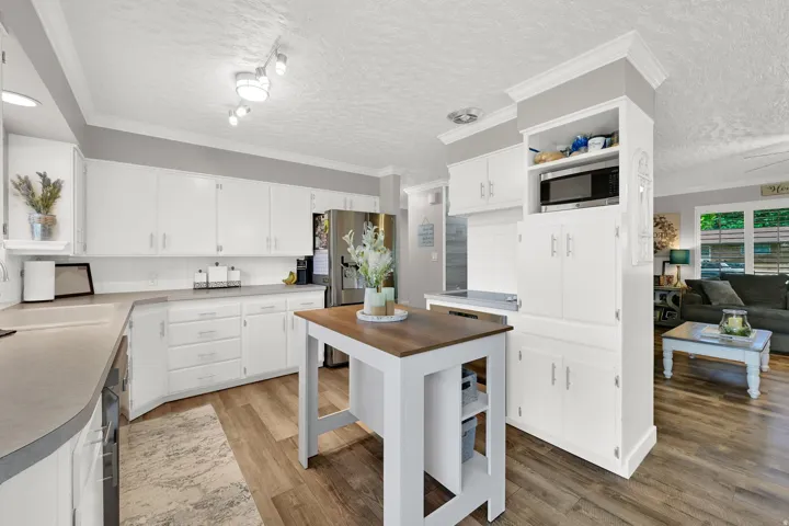 White cabinetry with brushed nickel hardware, wood-finish flooring, light-toned countertops, and built-in microwave