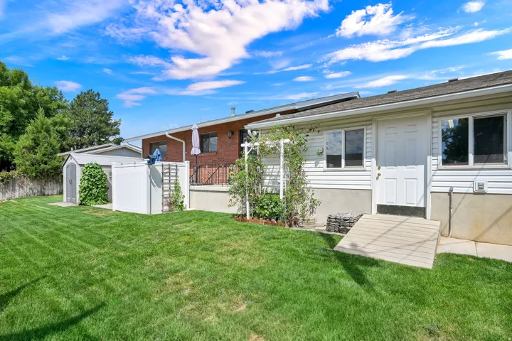 Expansive lawn, white siding exterior, storage shed, garden trellis, brick accent details