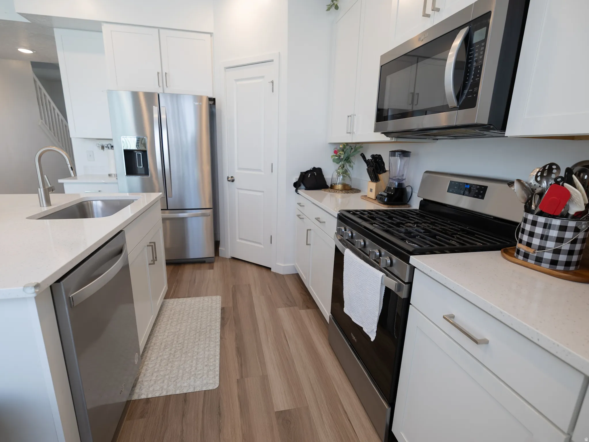 Modern kitchen featuring white cabinetry, stainless steel appliances, light-toned countertops, and wood-finish flooring