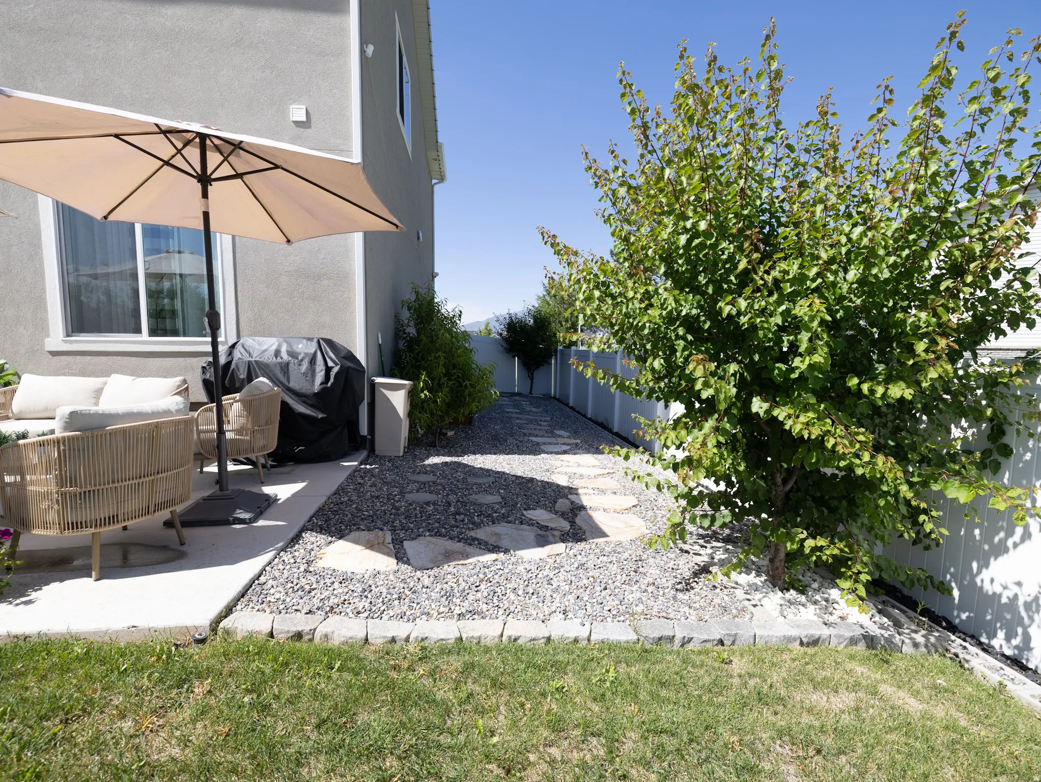 Paved patio area, gravel path with stepping stones, established landscaping, privacy fencing, stucco exterior