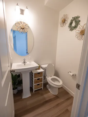 Pedestal sink with a polished chrome faucet, oval mirror, and wood-finish flooring