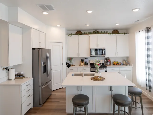 Kitchen featuring white cabinetry, stainless steel appliances, a center island with sink, light-toned countertops, and wood-finish flooring
