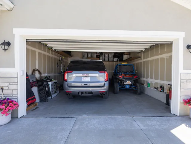 Attached two-car garage with concrete flooring, built-in shelving, and a textured exterior finish with stone accents
