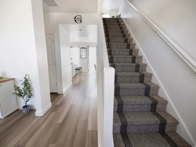Wood-finish flooring, white walls, and a staircase with a patterned carpet runner