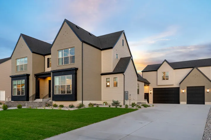 Contemporary exterior featuring light tan brick and siding, a dark roof, black-framed windows, and a concrete driveway