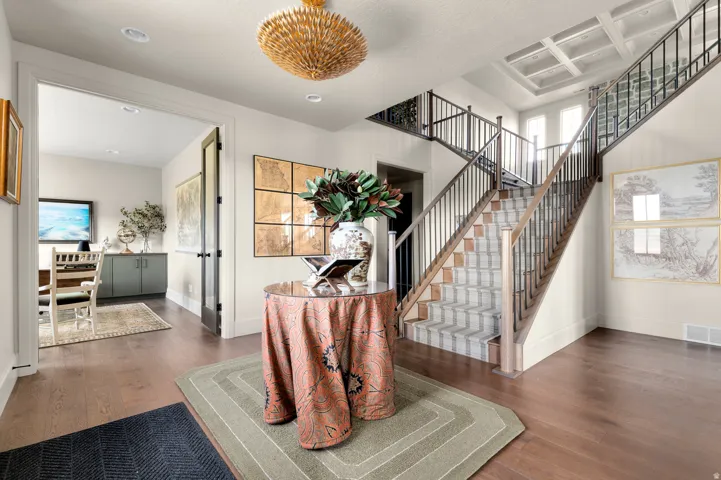 Hardwood flooring, wrought iron stair railing, coffered ceiling, recessed lighting, and a modern chandelier
