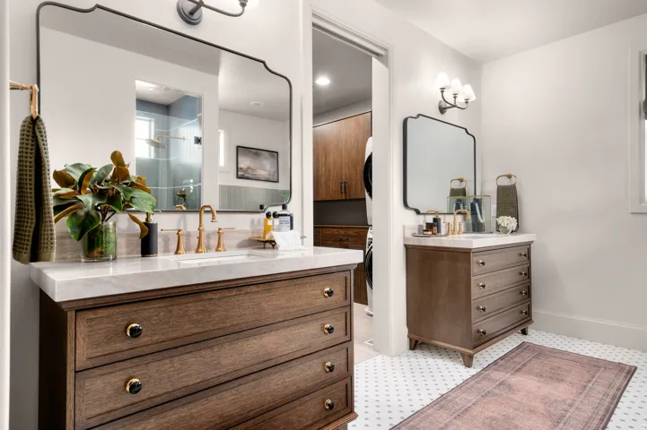 Dual vanities with wood-finish cabinetry, light stone countertops, and brass-finish fixtures