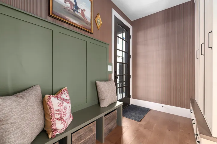 Wood-finish flooring, built-in storage bench, board and batten wall accent, paneled entry door, built-in cabinetry with dark hardware