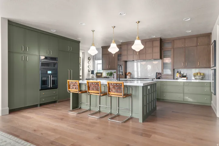 Kitchen featuring wood-finish flooring, two-tone cabinetry, a large island with integrated seating, built-in double ovens, and recessed lighting