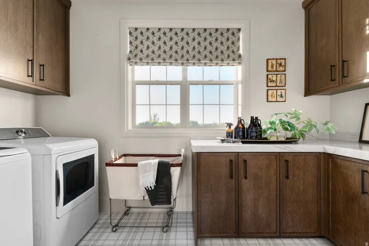 Window with divided lites, patterned roller shade, wood-finish cabinetry, white countertop, and plaid tile flooring