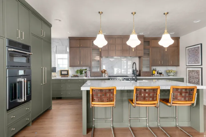 Integrated double wall ovens, wood-finish flooring, two-tone cabinetry, island with countertop, and decorative pendant lighting
