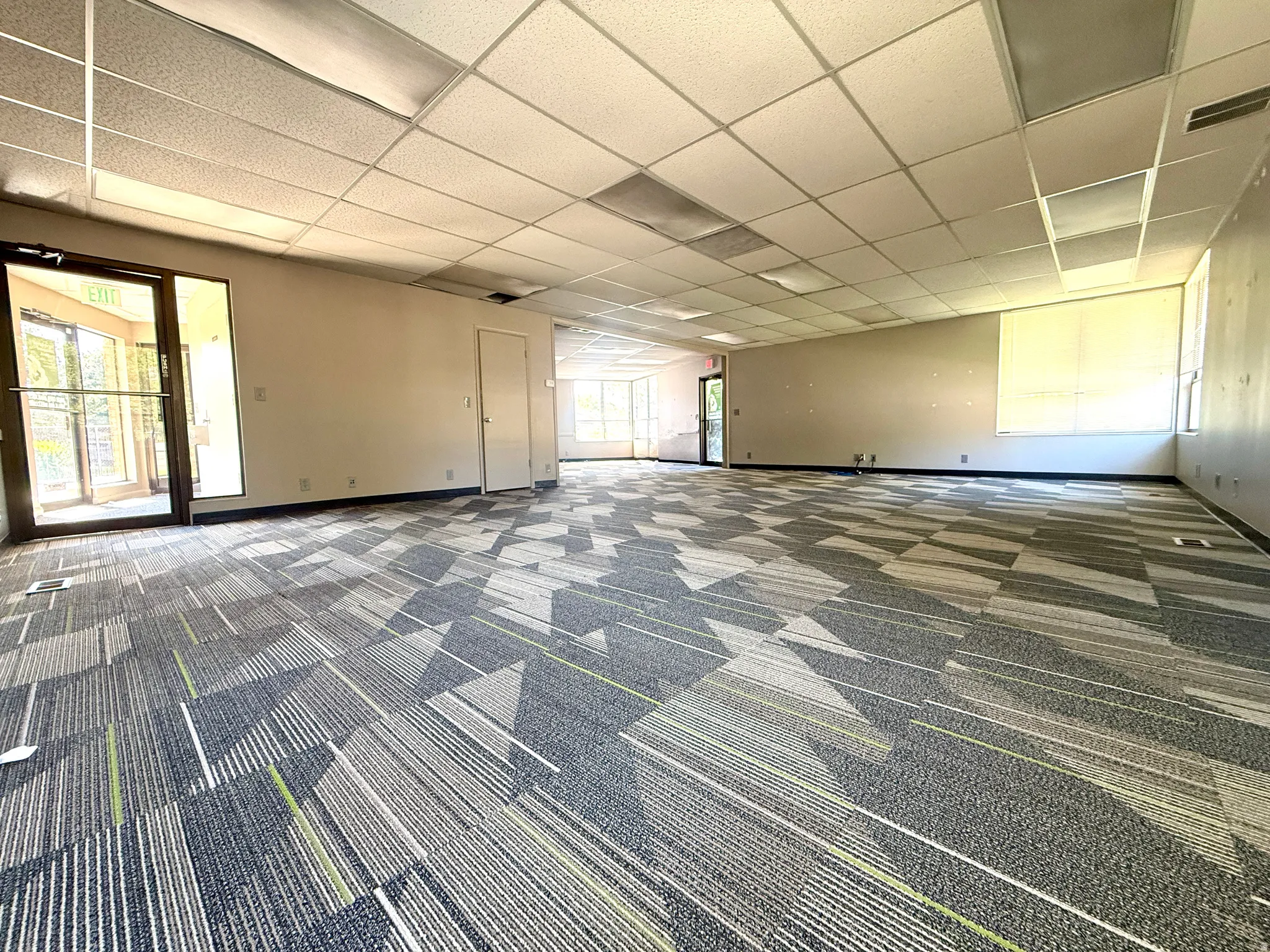 Spacious room featuring patterned carpet, multiple windows, a dropped ceiling with integrated lighting, and multiple entry points