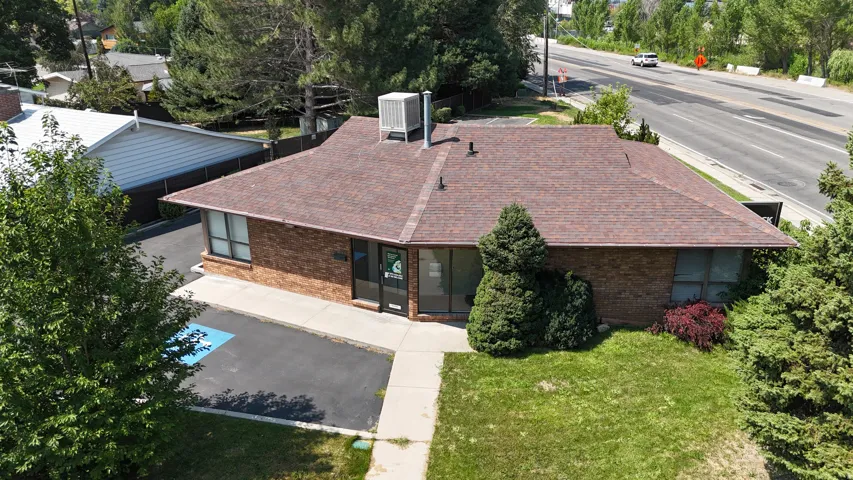 Brick-clad building with a shingle roof, paved parking area, and mature landscaping