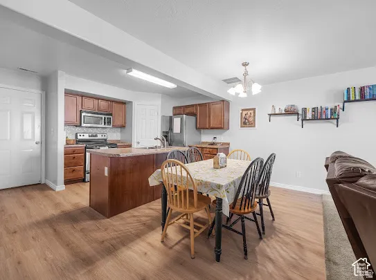 Open-concept living space featuring wood-finish flooring, a kitchen island with seating, dark wood cabinetry, a tile backsplash, and stainless steel appliances