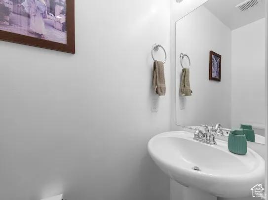 Pedestal sink with a chrome faucet, large wall mirror, and towel ring