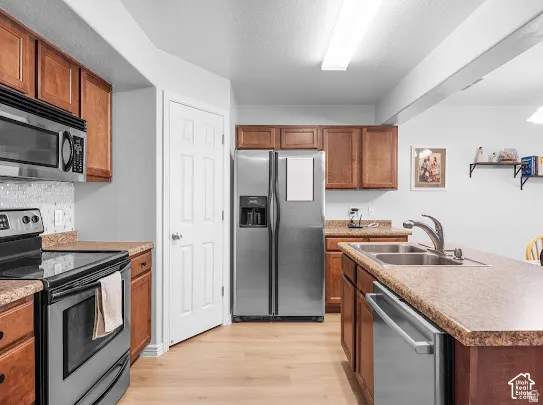 Wood-finish flooring, stainless steel appliances, upper and lower cabinetry, kitchen island with integrated sink, and white subway tile backsplash