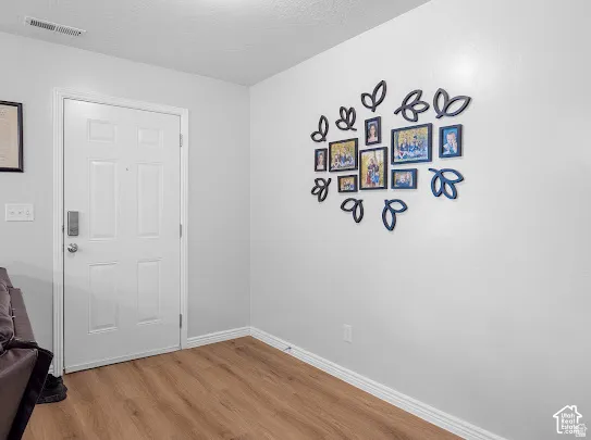 Wood-finish flooring with white trim and a paneled entry door featuring a smart lock
