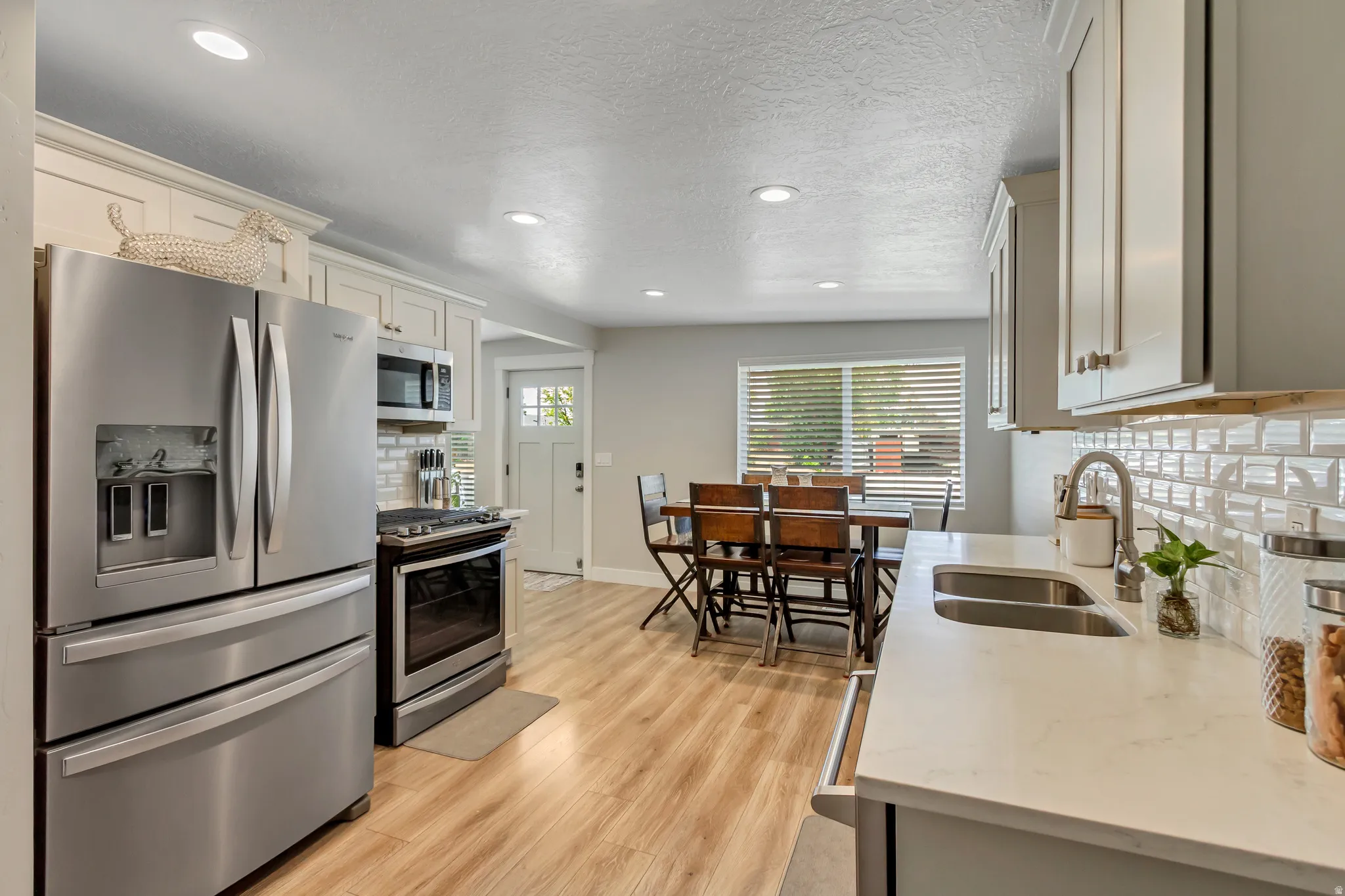 Contemporary kitchen featuring stainless steel appliances, light wood-finish flooring, white subway tile backsplash, white countertops, and recessed lighting