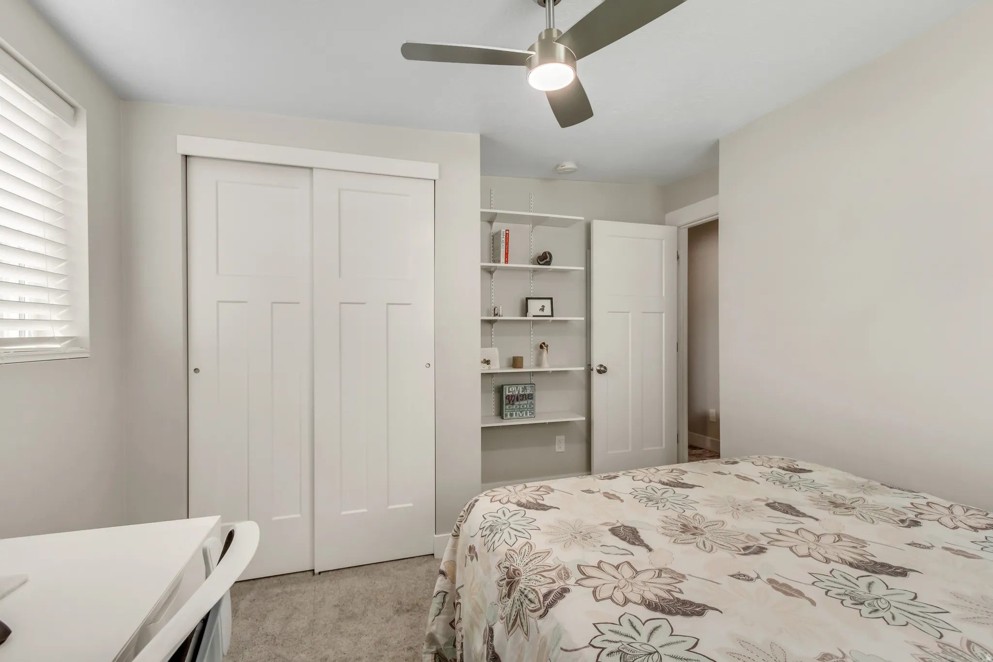 White sliding closet doors, built-in shelving, ceiling fan, and window with blinds