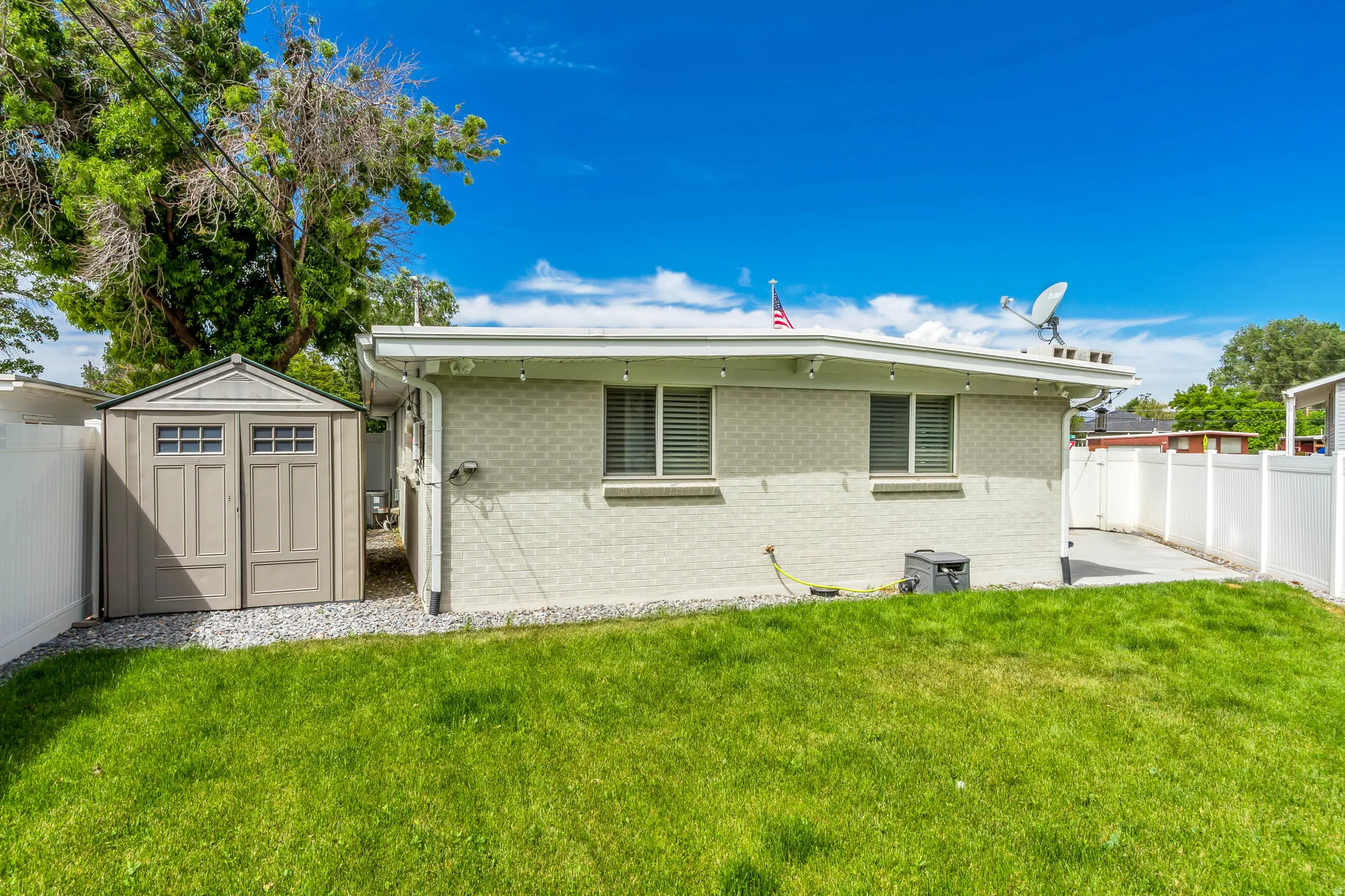 Expansive green lawn with a white vinyl privacy fence, a concrete patio, and an outdoor storage shed