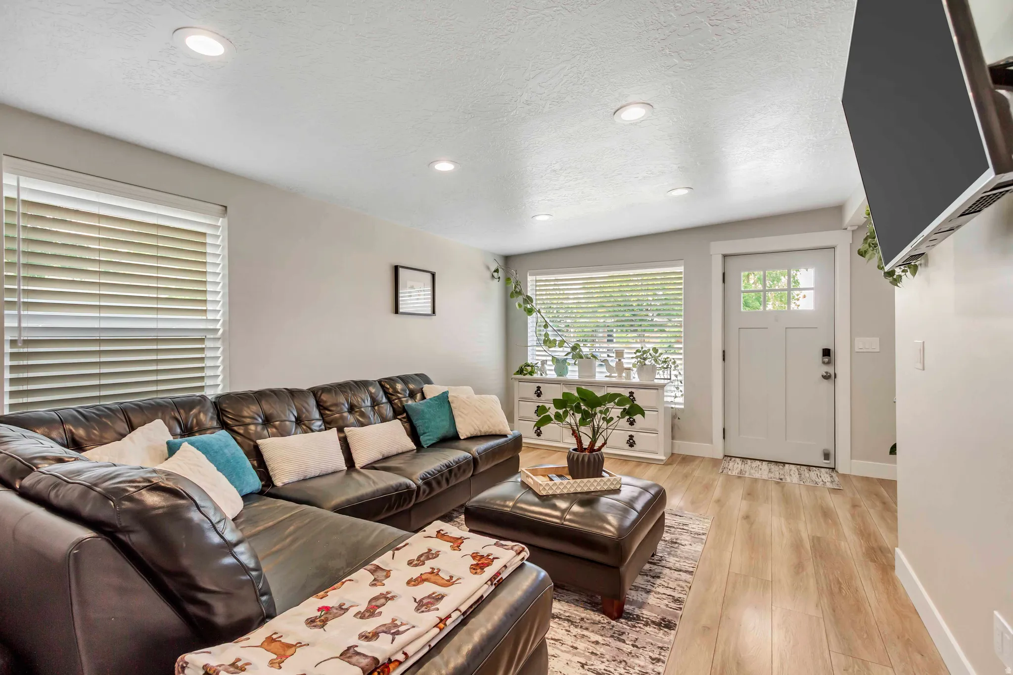 Recessed lighting illuminates this living space, featuring wood-finish flooring, a paneled entry door with glass inserts, and a window with horizontal blinds