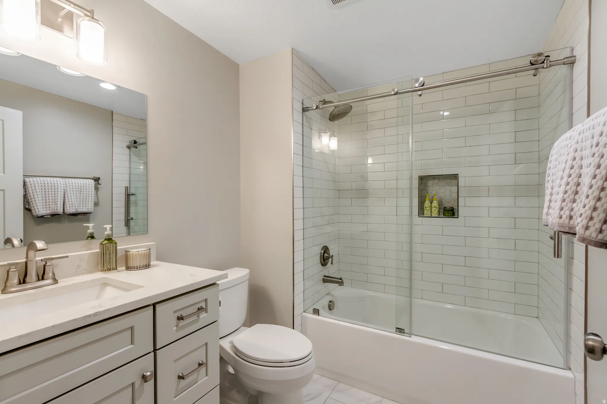 Vanity with light-colored countertop and undermount sink, brushed nickel fixtures, subway tile shower surround, glass sliding shower door, and recessed shower niche
