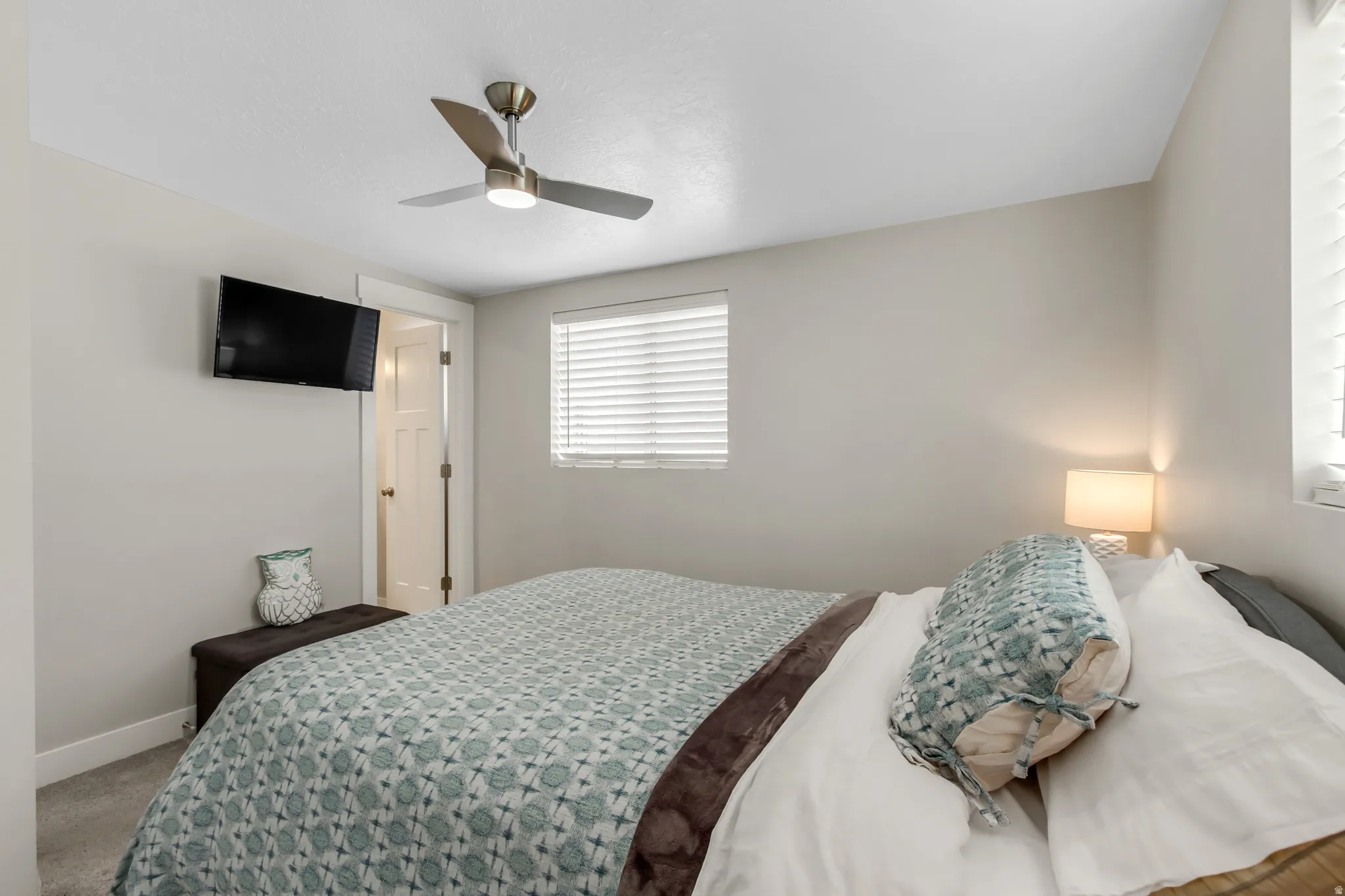 Recessed window with horizontal blinds, overhead ceiling fan with lighting, wall-mounted television, and a paneled door