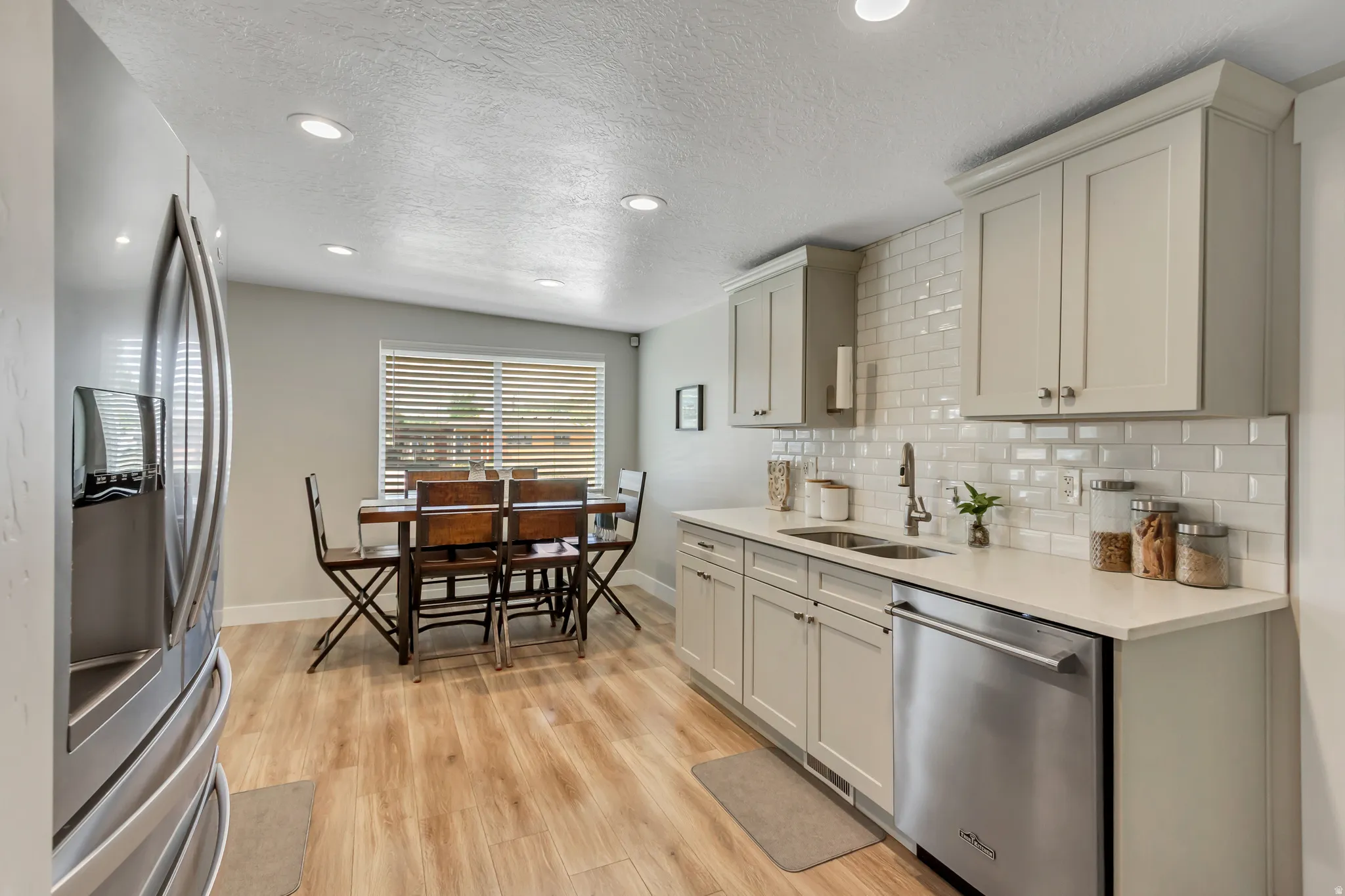 Kitchen featuring light-finish cabinetry, stainless steel appliances, a subway tile backsplash, and light-tone wood-finish flooring