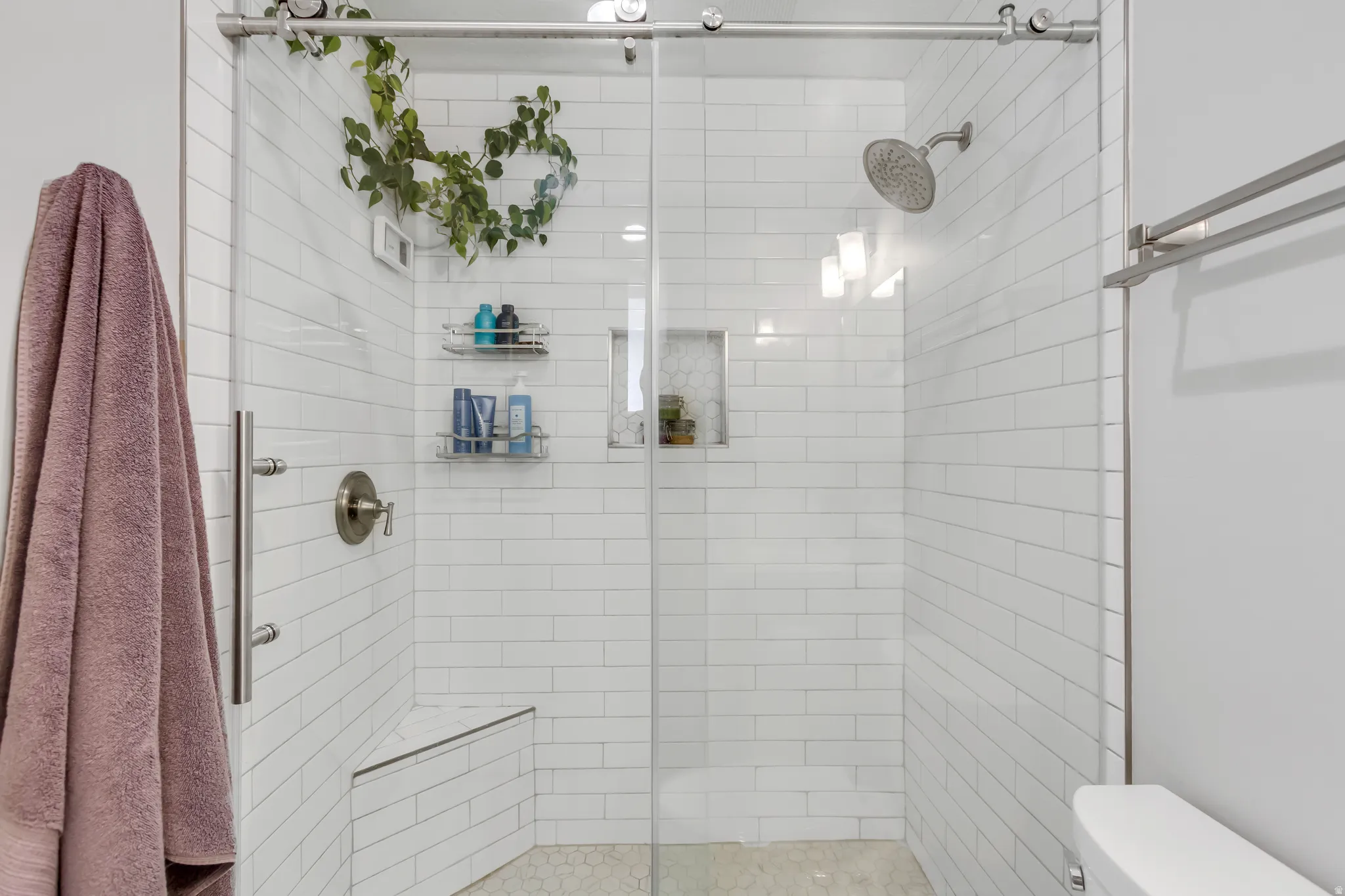 Frameless glass shower enclosure with subway tile surround, built-in bench seating, and hexagonal floor tile