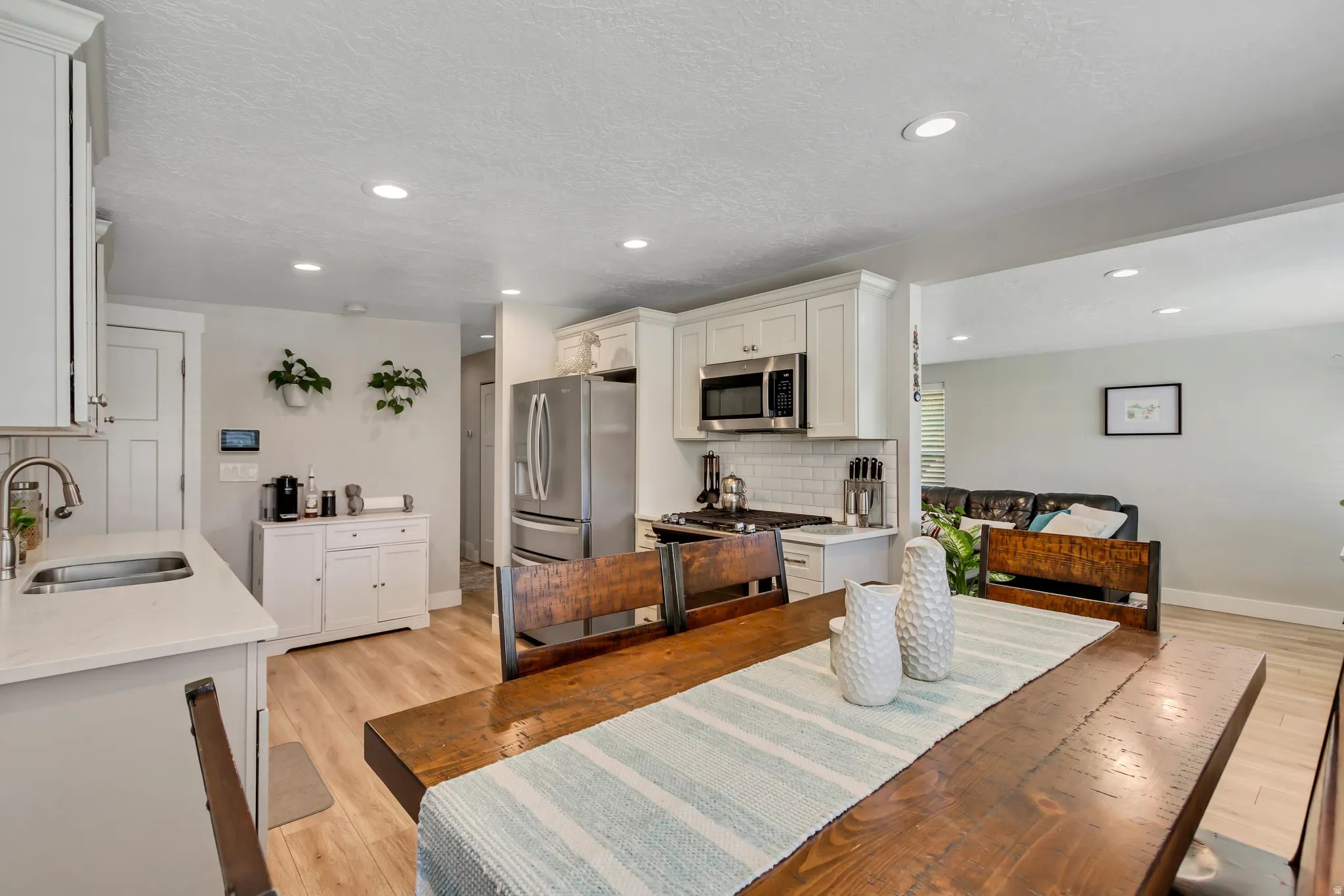 Wood-finish flooring, recessed lighting, white shaker-style cabinetry, stainless steel appliances, and a white subway tile backsplash
