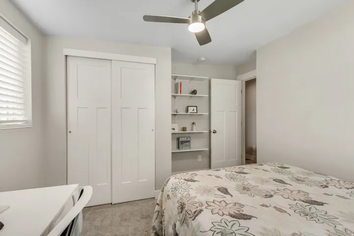 White sliding closet doors, built-in shelving, ceiling fan, and window with blinds