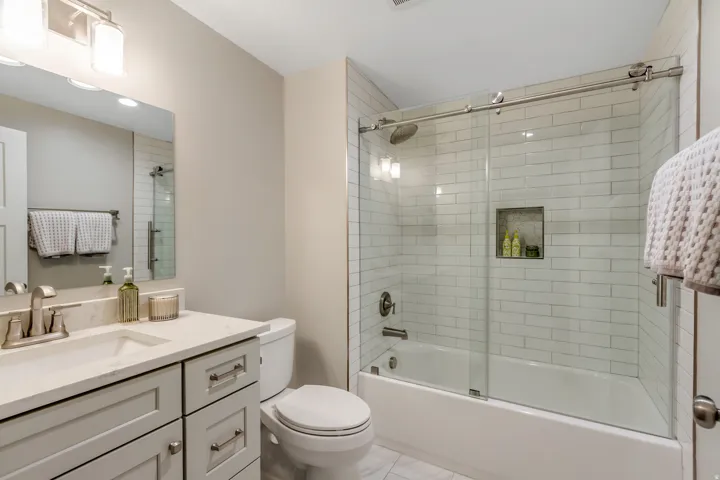 Vanity with light-colored countertop and undermount sink, brushed nickel fixtures, subway tile shower surround, glass sliding shower door, and recessed shower niche